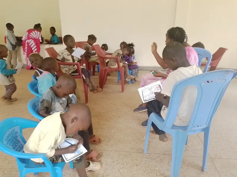 Children on plastic chairs working on Bible colouring sheets during a church mission